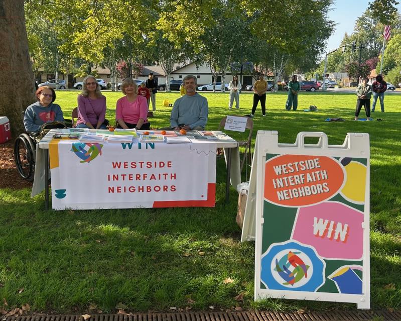 WIN community table at Welcome Beaverton, with banner and volunteers in a park.
